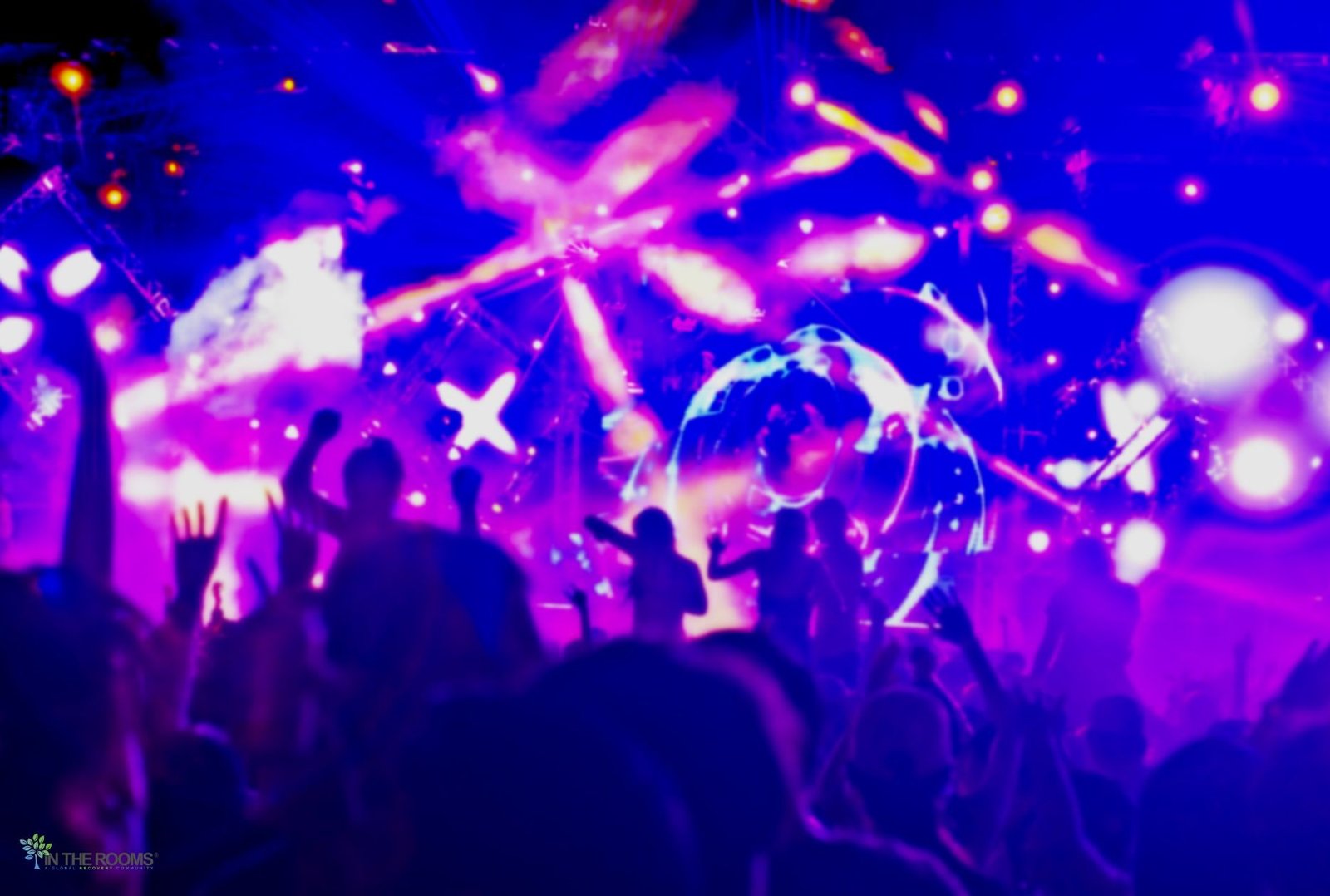 A crowded nightlife event with people raising their hands under colorful purple and blue stage lights.