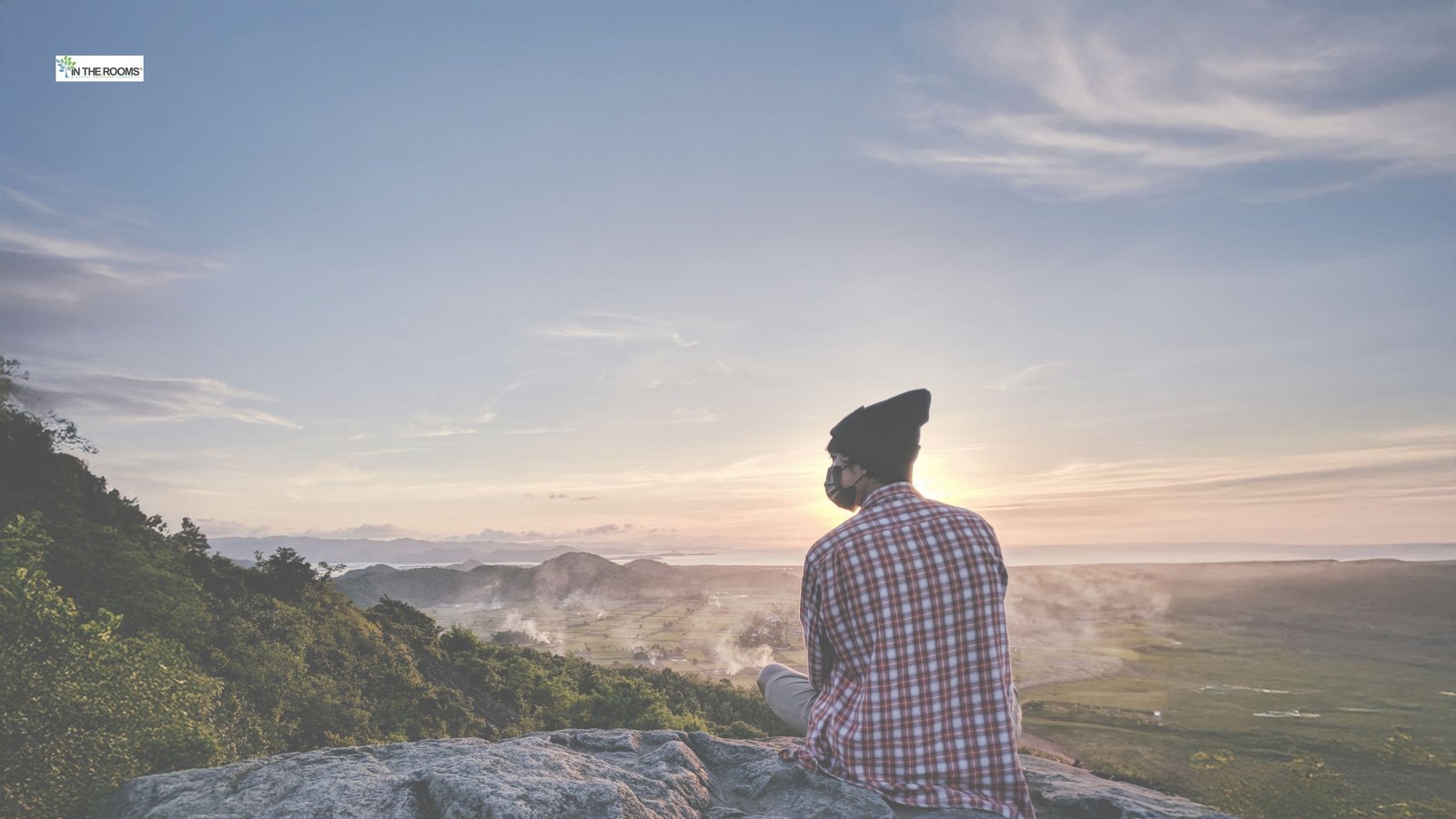 Person sitting quietly on a hill overlooking a wide landscape at sunrise, reflecting on recovery.