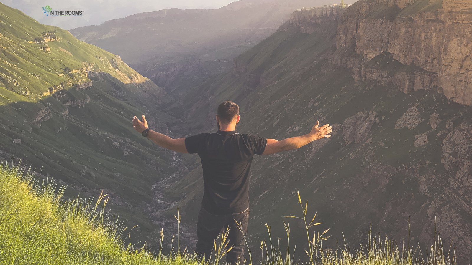 A person stands on a mountainside with arms outstretched, overlooking a vast valley, symbolizing strength, freedom, and personal growth in sobriety.