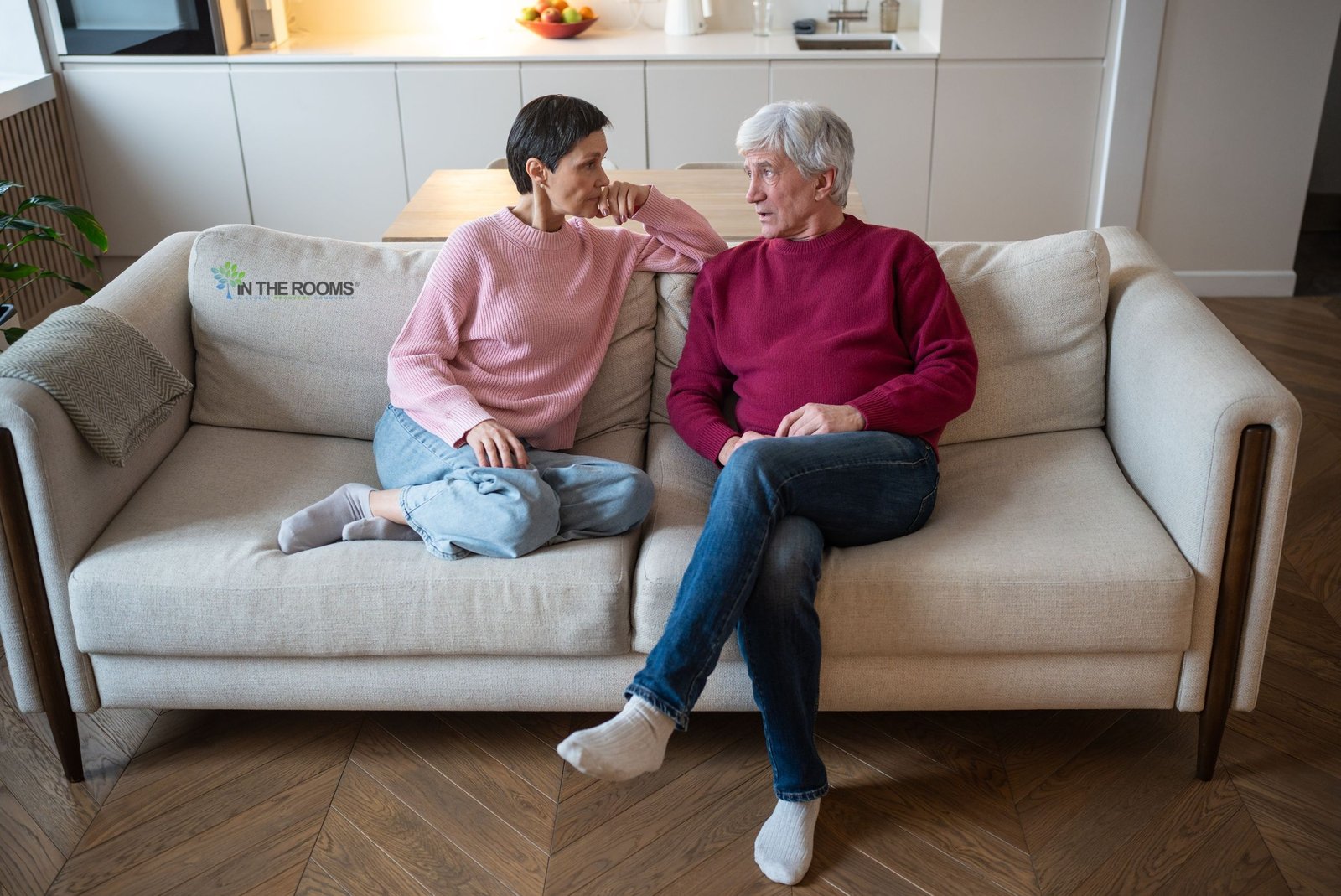 Two people sitting on a couch having a serious and supportive conversation about recovery and emotional healing.
