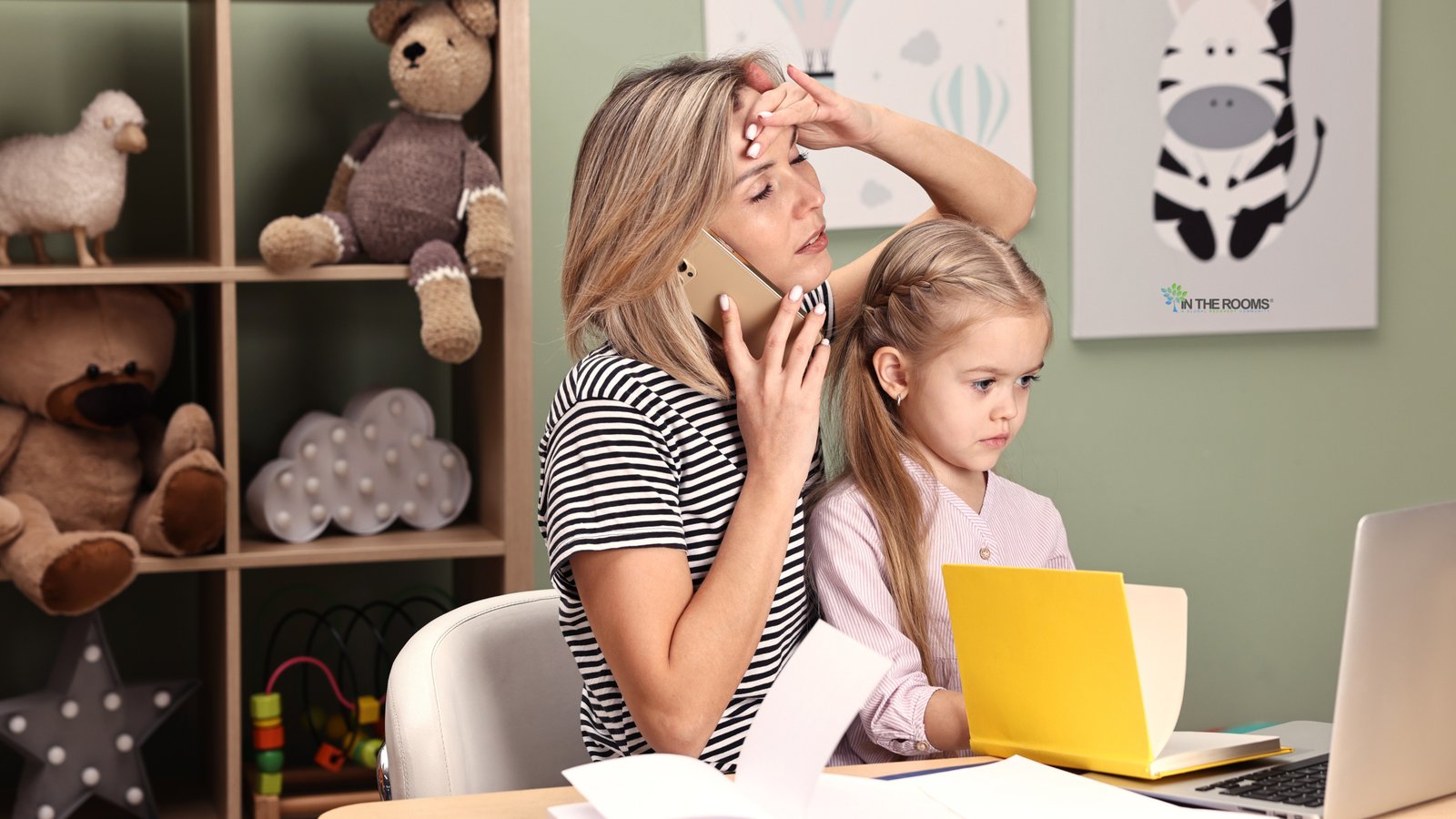 A stressed mother talking on the phone while managing work and childcare at home, reflecting financial and emotional pressure during recovery.