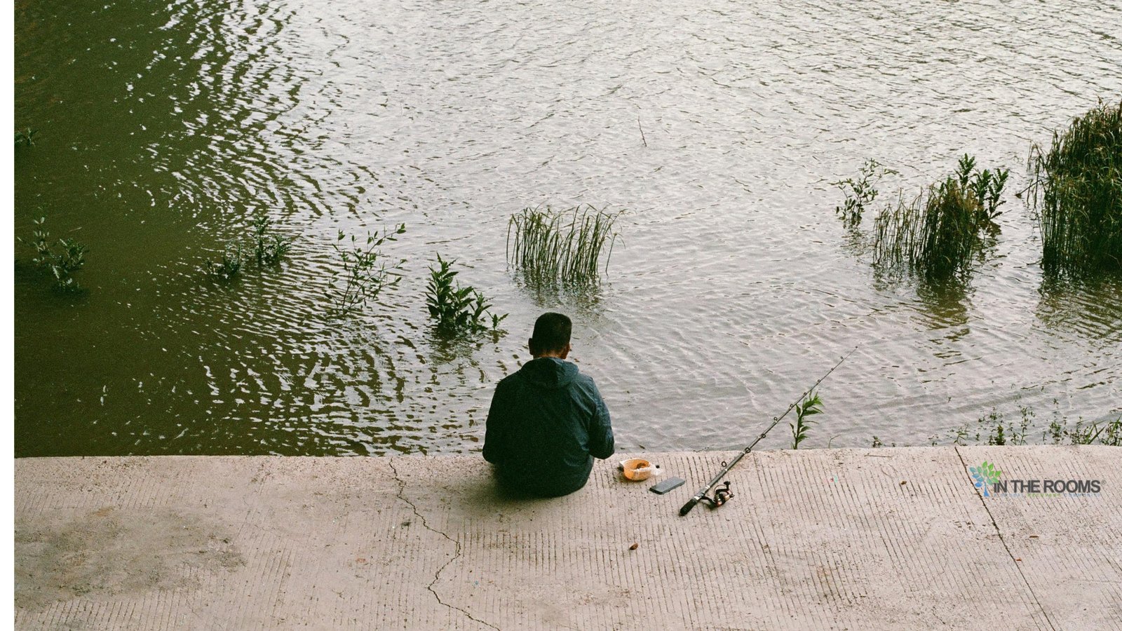 A person sitting quietly by the water with a fishing rod, reflecting on recovery and taking life one day at a time.
