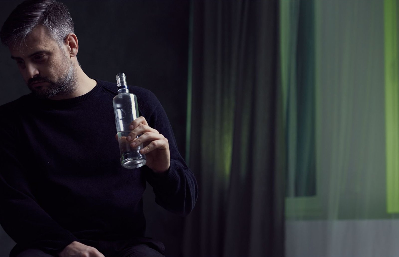 A man sits alone holding an empty bottle, reflecting on the challenges of addiction and the strength required to choose recovery.