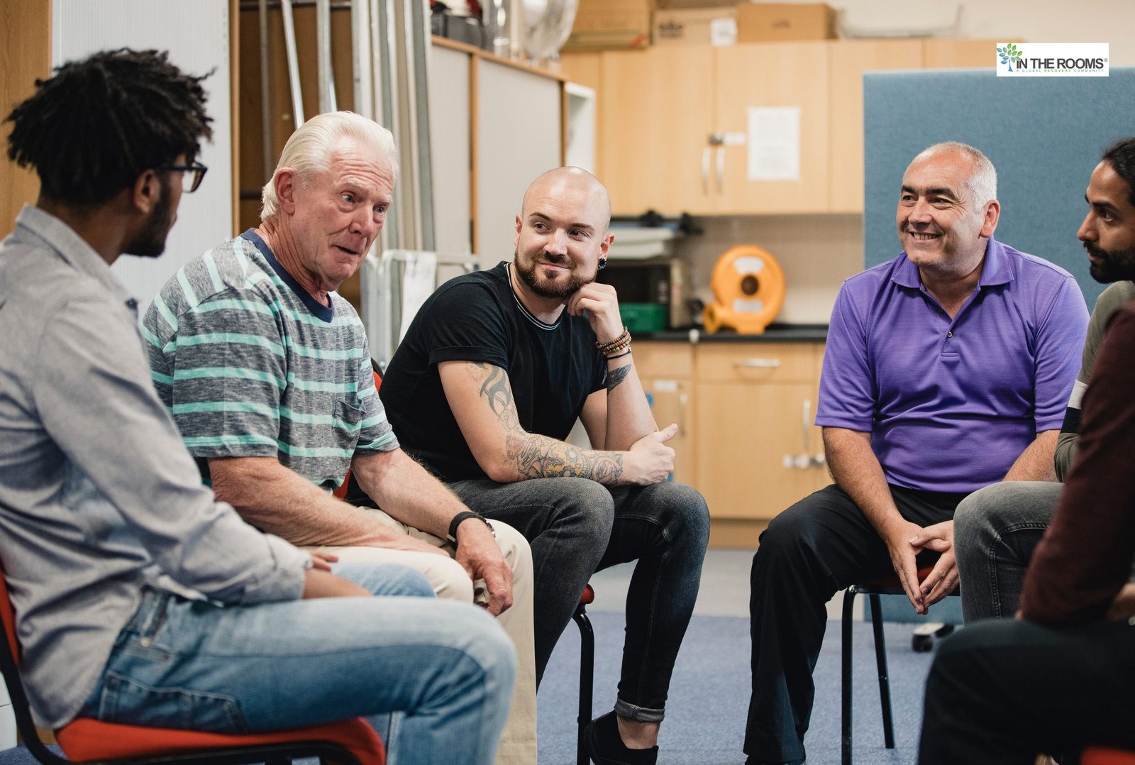 A diverse group of adults sitting in a circle and talking during a support group meeting, symbolizing connection, shared experience, and community support.